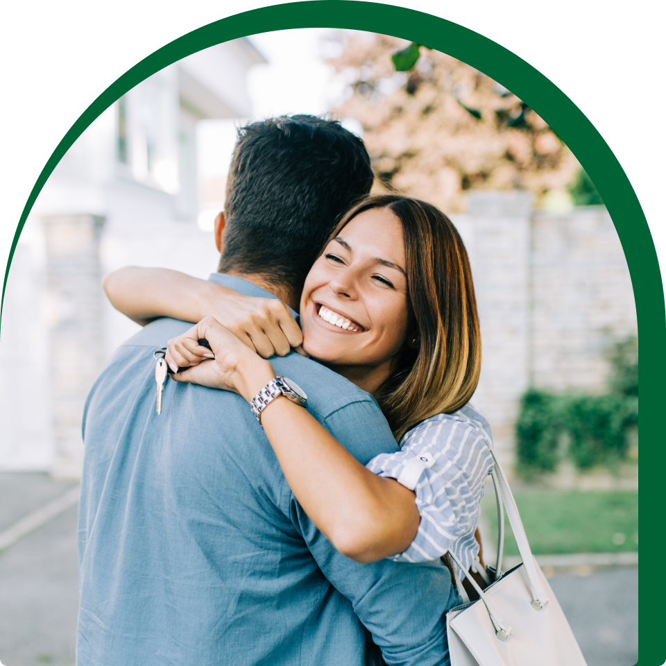 Happy couple hugging while holding house keys in front of their new home